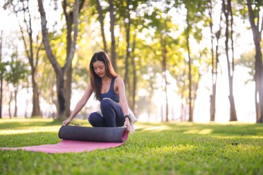 Genç Asyalı kadın dışarıda yoga seansına hazırlanıyor. Huzurlu park ortamında sağlık koşullarını kucaklamak. Sakin sabah egzersizi..