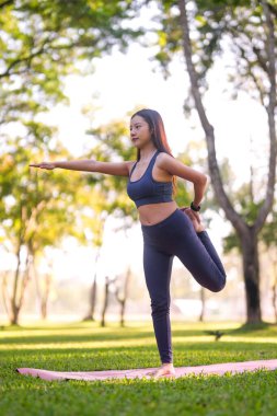 Genç Asyalı kadın huzur parkında yoga dengesi kuruyor. Zindelik sağlığını ve doğanın ortasında bilinçli egzersizi somutlaştırıyor..