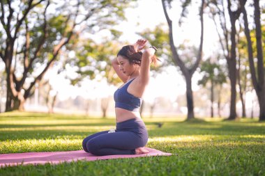 Asyalı kadın açık hava yogasına hazırlanıyor. O, huzurlu bir parkta bir paspasın üzerinde spor giysileri giyer. Sağlık ve refahı teşvik eder..