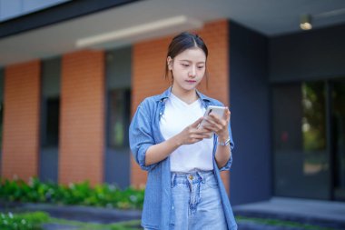 Asyalı genç bir kadın sosyal medya için aile ve arkadaşlarıyla iletişim kurmak için akıllı telefon kullanıyor. İnternet alışverişini iletişim teknolojisiyle tarıyorum..