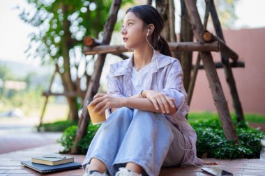 Düşünceli Asyalı genç bayan açık hava parkının kampüs ortamından hoşlanıyor. Laptop ve dizüstü bilgisayarın yanında müzik dinleyerek rahatlıyorum. Öğrenci yaşam tarzı konsepti.