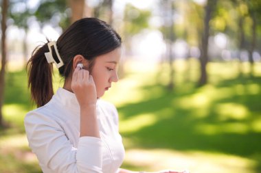 Genç Asyalı yetişkin, kablosuz kulaklık ayarlama egzersizi için hazırlanıyor. Sağlıklı yaşam tarzını benimsiyor, müzikten zevk alıyor..