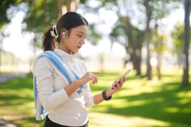 Dişi sporcu egzersiz verilerini takip etmek için mobil cihaz kullanıyor. Kablosuz kulaklıkların keyfini çıkarın.