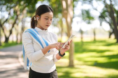 Genç Asyalı kadın gezici araç parkına göz atıyor. Spor kulaklıkları takıyor. Sağlık durumunu destekleyen spor aktiviteleri için hazır..