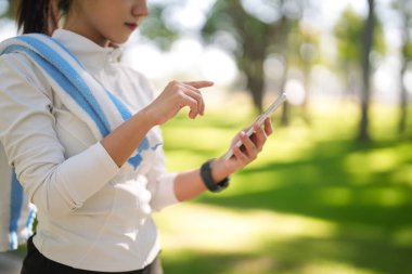 Genç Asyalı kadın idmandan sonra cep telefonundan sağlık durumunu kontrol ediyor. Doğal bir ortamda açık hava fitness ve dijital sağlık yönetimini kucaklamak.