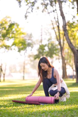Genç Asyalı kadın dışarıda egzersiz paspası hazırlıyor. Sakin bir yer. Sağlıklı yaşam tarzı.