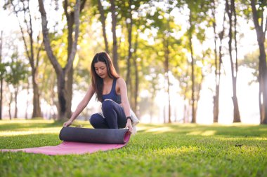 Genç Asyalı kadın dışarıda yoga seansına hazırlanıyor. Huzurlu park ortamında sağlık koşullarını kucaklamak. Sakin sabah egzersizi..