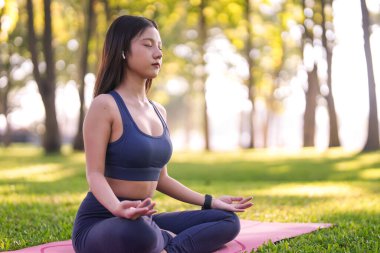 Asian woman practices deep meditation outside in a peaceful nature setting achieving mental serenity and physical harmony. Focus mind.
