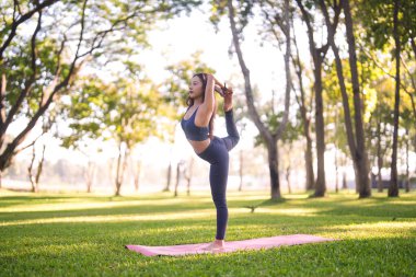 Yetişkin Asyalı kadın dışarıda yoga poziyonu veriyor. Bu huzurlu görüntü, barışın vücut kontrolünü ve zihinsel refahı temsil ediyor. Mükemmel sağlık motivasyonu.