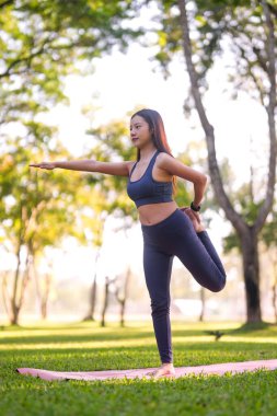 Genç Asyalı kadın huzur parkında yoga dengesi kuruyor. Zindelik sağlığını ve doğanın ortasında bilinçli egzersizi somutlaştırıyor..