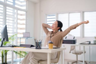 Yetişkin Asyalı kadın profesyonel, ferahlatıcı bir iş molası için parlak modern çalışma sahasında kollarını esnetmekten zevk alıyor.