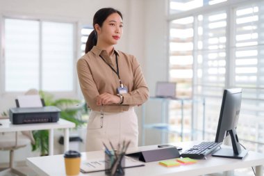 Kendine güvenen Asyalı yetişkin kadın yönetici, açık vizyonlu çalışma alanını gözlemliyor. Gündüz ofis işlerini yürütüyor.