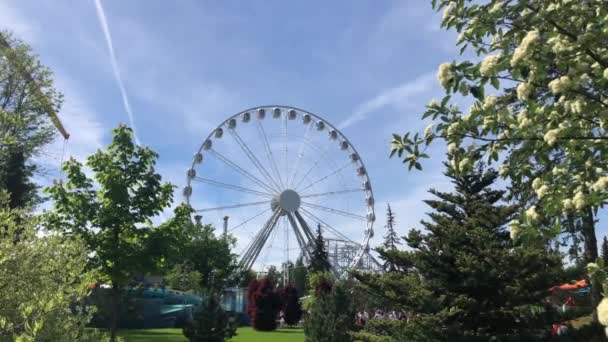 Saint Petersburg, Russia - 2 June 2021: Ferris wheel in an amusement park rotates against a clear blue sky with tourist people walking, Illustrative Editorial — Αρχείο Βίντεο