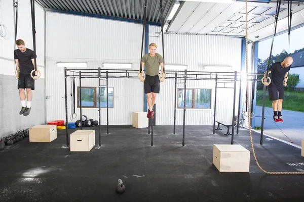 Three well trained men exercising dips with rings