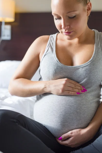 Femme enceinte s'assoit sur le lit avec ses mains au ventre — Photo