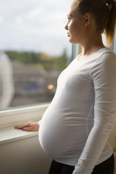 Thoughtful pregnant woman looking out the window — Stock Photo, Image