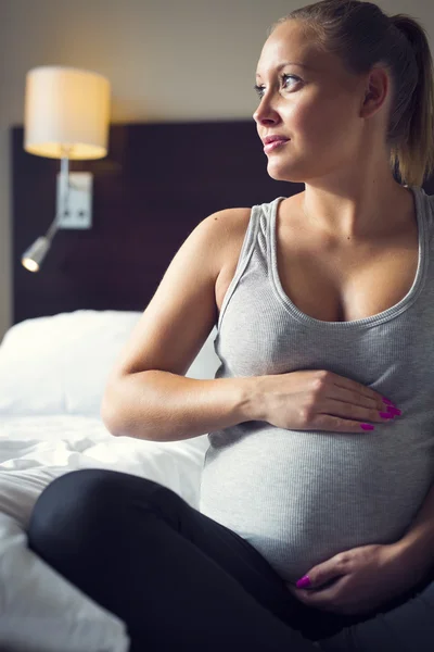 Femme enceinte s'assoit sur le lit avec sa main au ventre — Photo