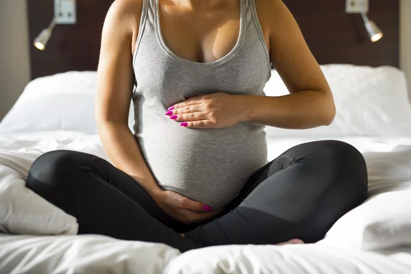 Беременная женщина сидит на кровати с рукой на животе — стоковое фото