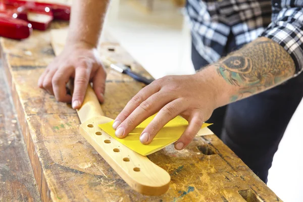 Carpintero lijando un cuello de guitarra en madera en el taller — Foto de Stock