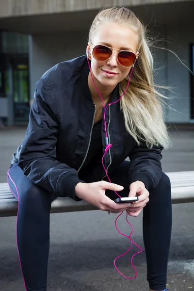 Mujer sonriente con gafas de sol se sienta al aire libre y utiliza el teléfono —  Fotos de Stock