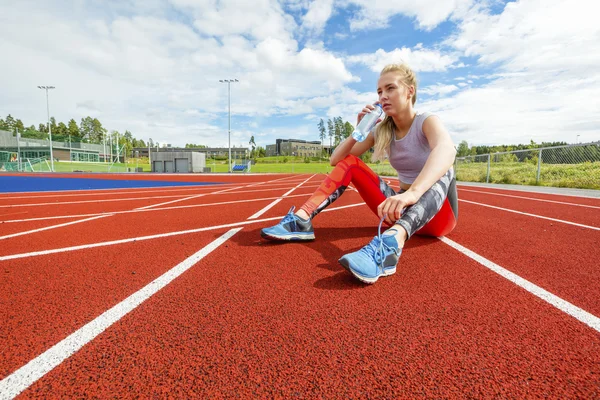 Ung kvinna dricksvatten och vilar på löparbanor — Stockfoto