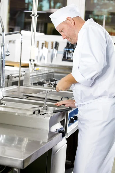 Cocinero enfocado freír alimentos en freidora en gran cocina industrial — Foto de Stock