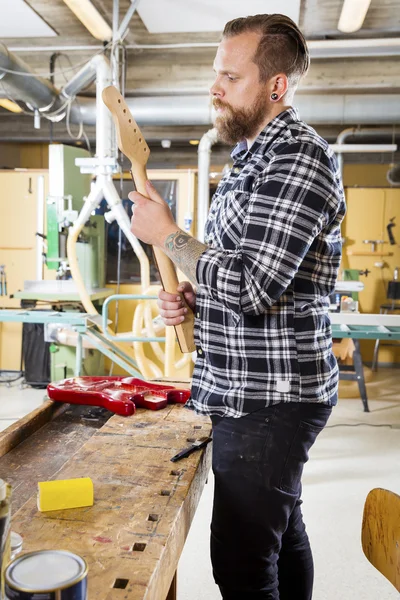 Timmerman inspecteert een houten gitaar hals in werkplaats — Stockfoto