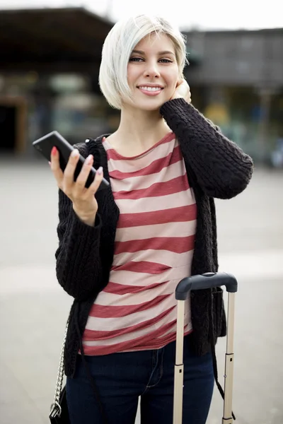 Sorrindo jovem mulher segurando telefone inteligente fora da estação ferroviária — Fotografia de Stock