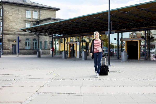 Kobieta z kołowych bagażu chodzenie zewnątrz dworca — Zdjęcie stockowe
