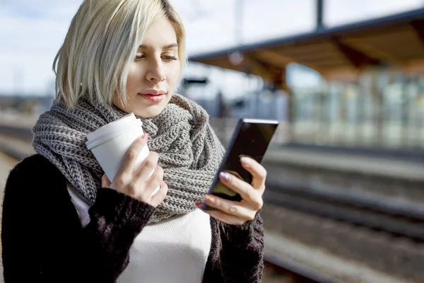 Kvinna med kaffekopp med mobiltelefon Train Station — Stockfoto