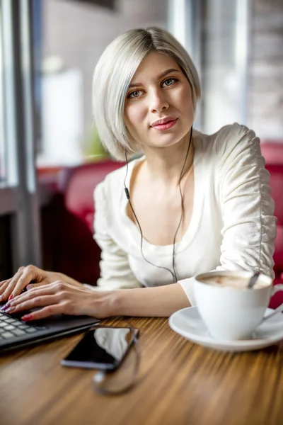 Ung kvinna lyssna musik medan du arbetar med Laptop i Cafe — Stockfoto