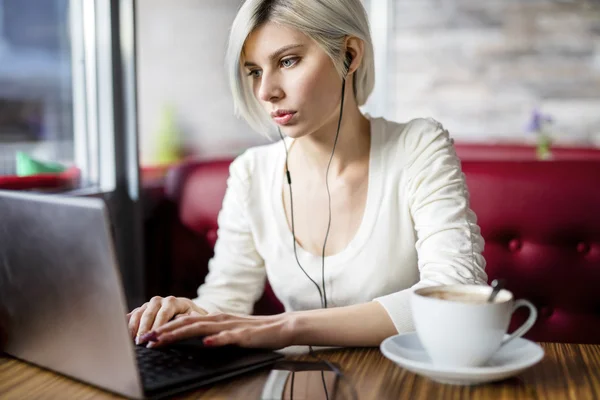 Mujer escuchando música mientras trabaja en el ordenador portátil en el café —  Fotos de Stock