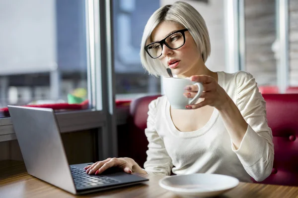 Mujer tomando café mientras trabaja en el ordenador portátil en el café — Foto de Stock