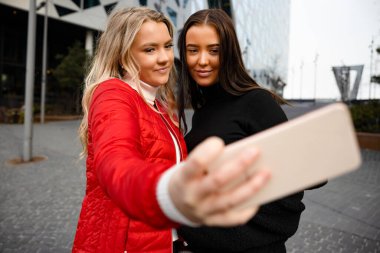 İki Gülümseyen Güzel Arkadaş Şehirde Smartphone ile Selfie Çekiyor