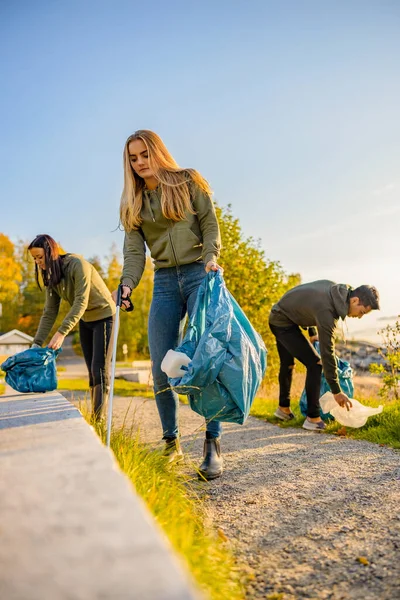 Jóvenes voluntarios recogiendo basura en bolsa en el parque — Foto de Stock