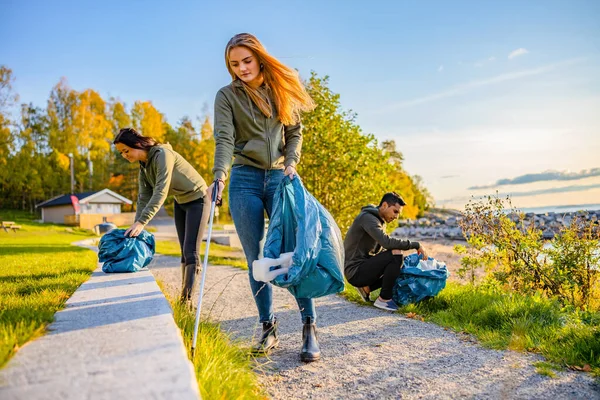 Equipo de voluntarios recogiendo basura en una bolsa en la playa — Foto de Stock