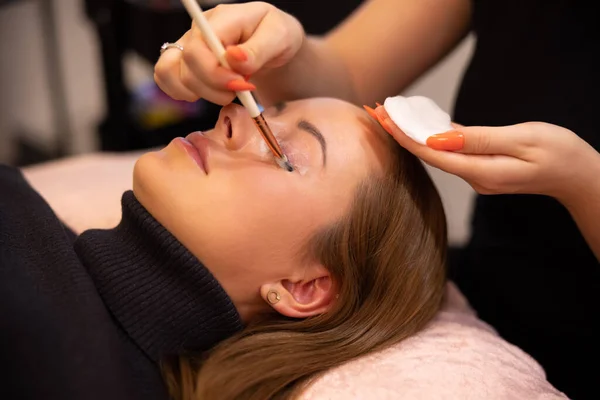 Manos del cosmetólogo que aplica la crema en el párpado femenino de los clientes — Foto de Stock