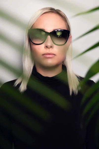 Primer plano de la mujer con gafas de sol escondidas detrás de hojas de palmeras tropicales — Foto de Stock