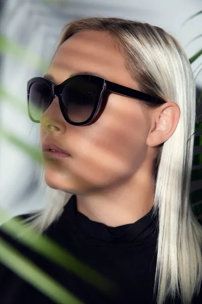 Hermosa mujer con gafas de sol escondidas detrás de hojas de palmeras tropicales — Foto de Stock