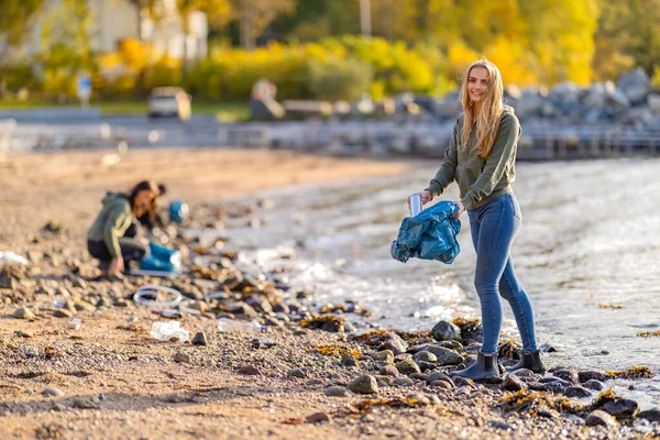 在阳光明媚的日子，热心微笑的年轻义工在海滩清洁塑料 图库照片