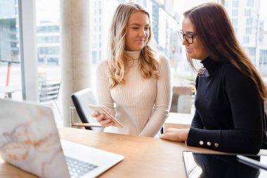 Kafedeki Masa 'da Dizüstü bilgisayar ve akıllı telefon kullanan iki Neşeli Kadın Blogcu