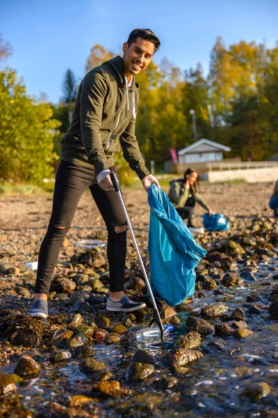 Hombre sonriente limpiando el océano con voluntarios en un día soleado —  Fotos de Stock