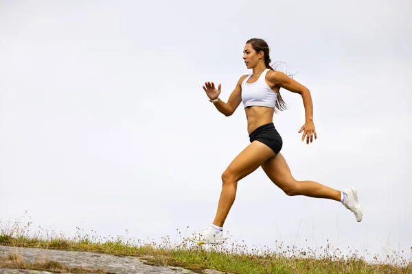 Deportista femenina decidida a correr en la montaña contra el cielo —  Fotos de Stock