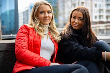 Portrait Of Two Smiling Female Best Friends Sitting In City