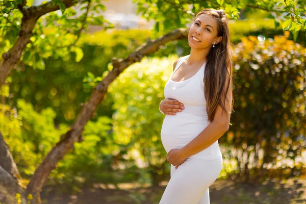 Lächelnde Schwangere steht im Garten und hält sich den Bauch — Stockfoto