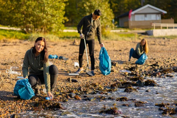 一个小组的年轻女子在海滩捡塑料袋里的垃圾 免版税图库照片