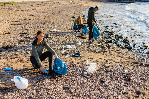 Mujer dedicada en un equipo recogiendo basura plástica en bolsa en la playa —  Fotos de Stock