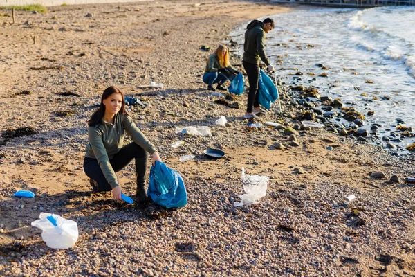 在海滩，一个团队中的专职人员在袋子里捡拾塑料垃圾 图库图片