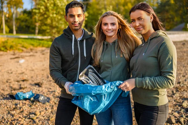 Une équipe souriante de bénévoles tenant un sac poubelle à la plage — Photo