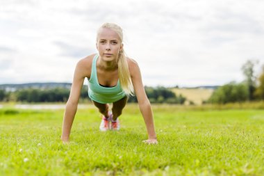 Parkta şınav çeken genç bir kadın.